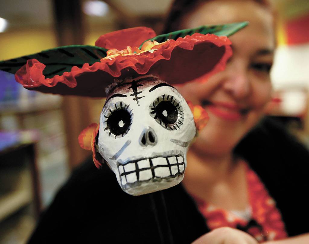 Helping set up a Dia de los Muertos display in the Lynnwood Library was Lupita Zamora, who holds up a skeleton head on a stick. (Dan Bates / The Herald)