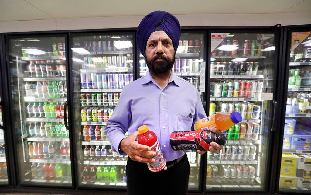 In this Oct. 1 photo, shop owner Prem Singh holds several soft drinks as he poses for a photo in front of a drink cooler in his convenience store in Kent. (AP Photo/Elaine Thompson, file)