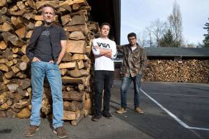 Shane McDaniel and his twin sons, Harrison and Henry, 20, stand by the wood stacked in front of their Lake Stevens home. They started with 40 cords of wood and are giving it out to those in need. The men spent months chopping the wood with the help of several friends. (Andy Bronson / The Herald)
