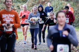 Finding two along the course, Brooklyn Hill and Katie Clark run with frozen turkeys during the Turkey Trot 5K on Thursday Arlington. Runners could keep the turkey if they finished the race with it in hand. (Andy Bronson / The Herald)