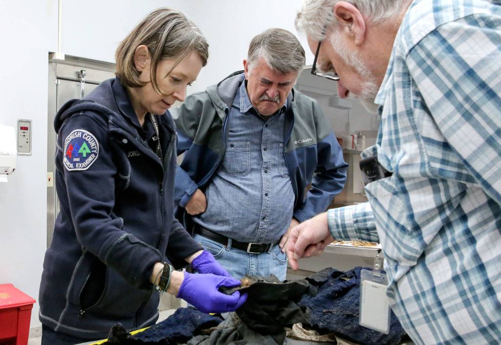 Cold case investigator Jane Jorgensen, left, retired judge and prosecutor Ken Cowsert, center, and mental health professional Chuck Wright look over remnants of clothing Nov. 13, at the Snohomish County Medical Examiners Office. (Kevin Clark / The Herald)
