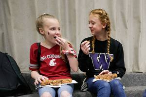 Sporting opposing team gear, Lauren Rice and Avery Kirkman, right, enjoy chatting together as Dutch Hill Elementary held an Apple Cup-themed Dads and Donuts event, with the gym decked out in Cougar and Husky colors, on Wednesday, Nov. 21, 2018 in Snohomish, Wa. (Andy Bronson / The Herald)