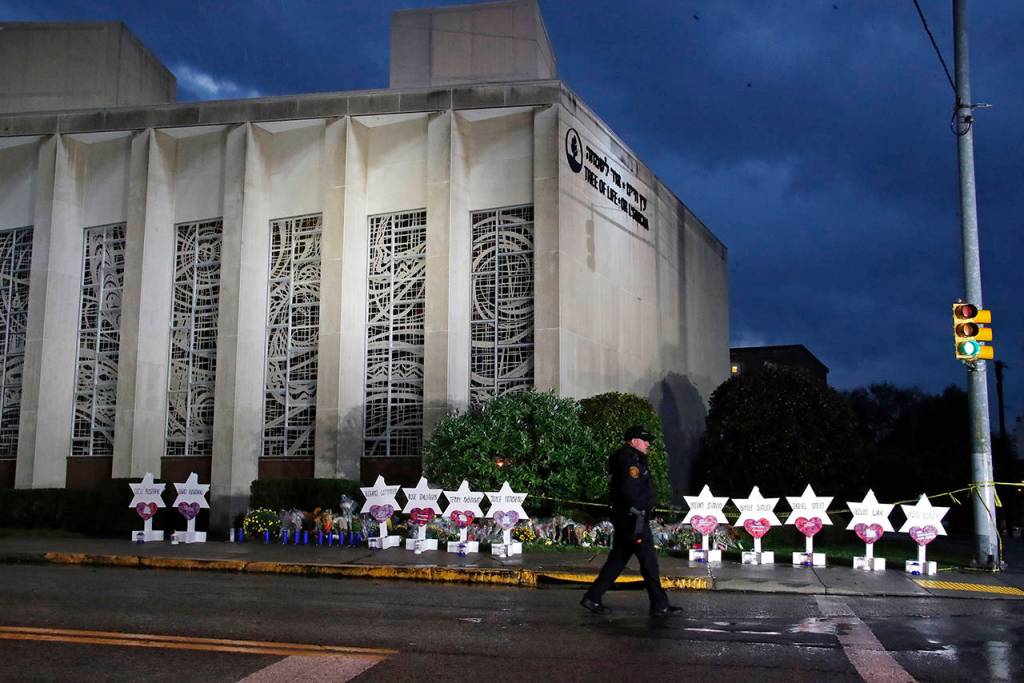 In this Oct. 28 photo, a Pittsburgh Police officer walks past the Tree of Life Synagogue and a memorial of flowers and stars in Pittsburgh in remembrance of those killed and injured when a shooter opened fire during services Saturday at the synagogue. (AP Photo/Gene J. Puskar, File)