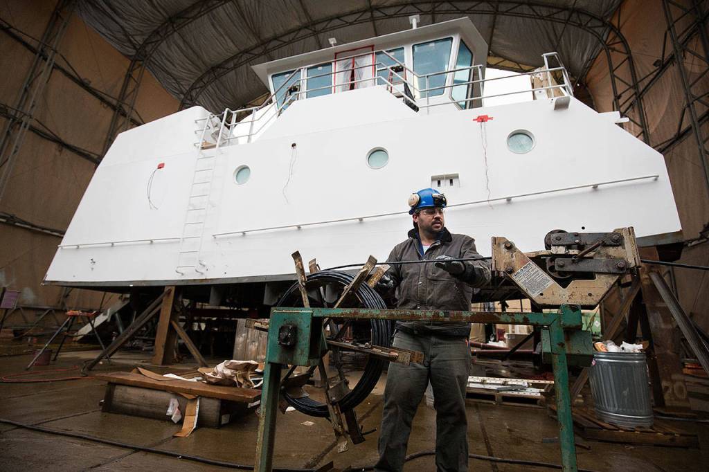 Turning a spool that looks like an old ships wheel, electrician Levi Egerton measures out cable for lighting in a tug pilothouse at Nichols Brothers Boat Builders. (Andy Bronson / The Herald)