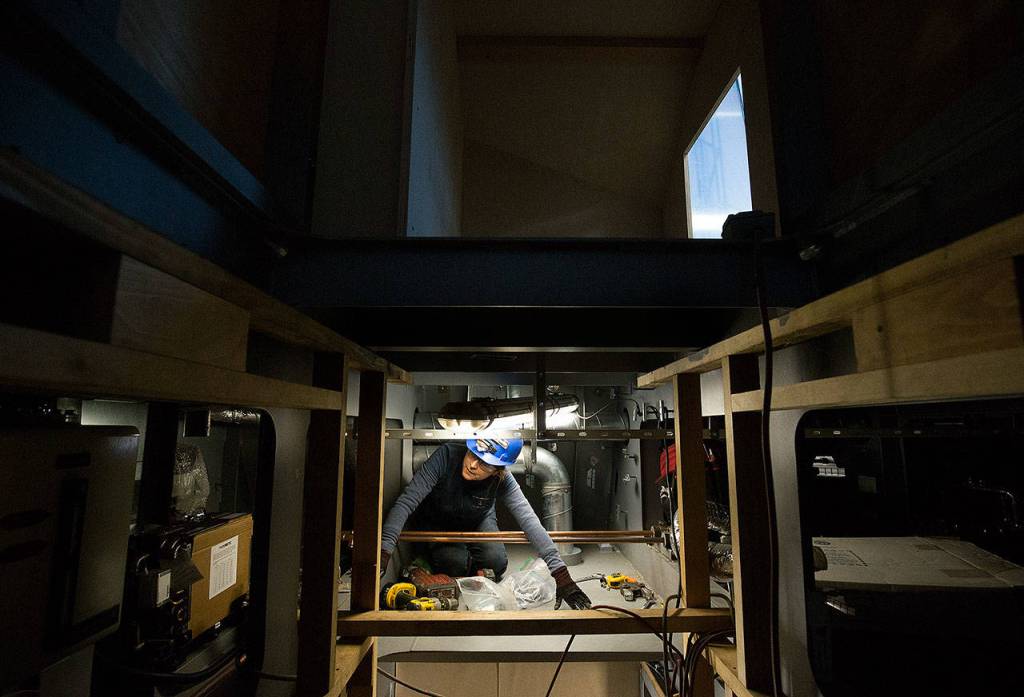 In the space between the ceiling and floor, Liliana Beltran crawls through tight spots while wiring a pilothouse at Nichols Brothers Boat Builders. (Andy Bronson / The Herald)