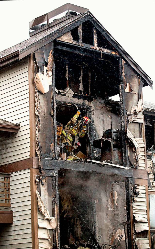 A firefighter works on a burned apartment above the unit where 3-year-old twin girls were rescued by two Everett Firefighters who crawled on the floor through thick smoke, heat and flames to save their lives. (Andy Bronson / Herald file)