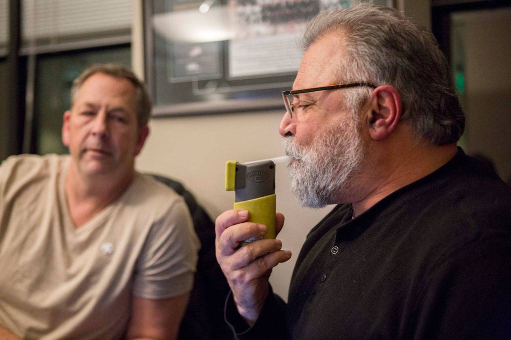 Lynnwood police officer Mark Brinkman watches as Maury Eskenazi blows into a breath test at the KRKO radio office in Everett. (Olivia Vanni / The Herald)
