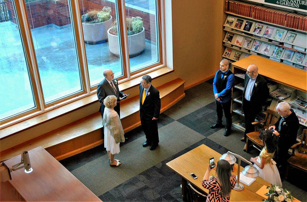In the spacious west-facing reading area of the Everett Library overlooking Port Gardner, officiant David Cooper performs the wedding for Gaylen Blue and Ed Wada. (Everett Public Library)