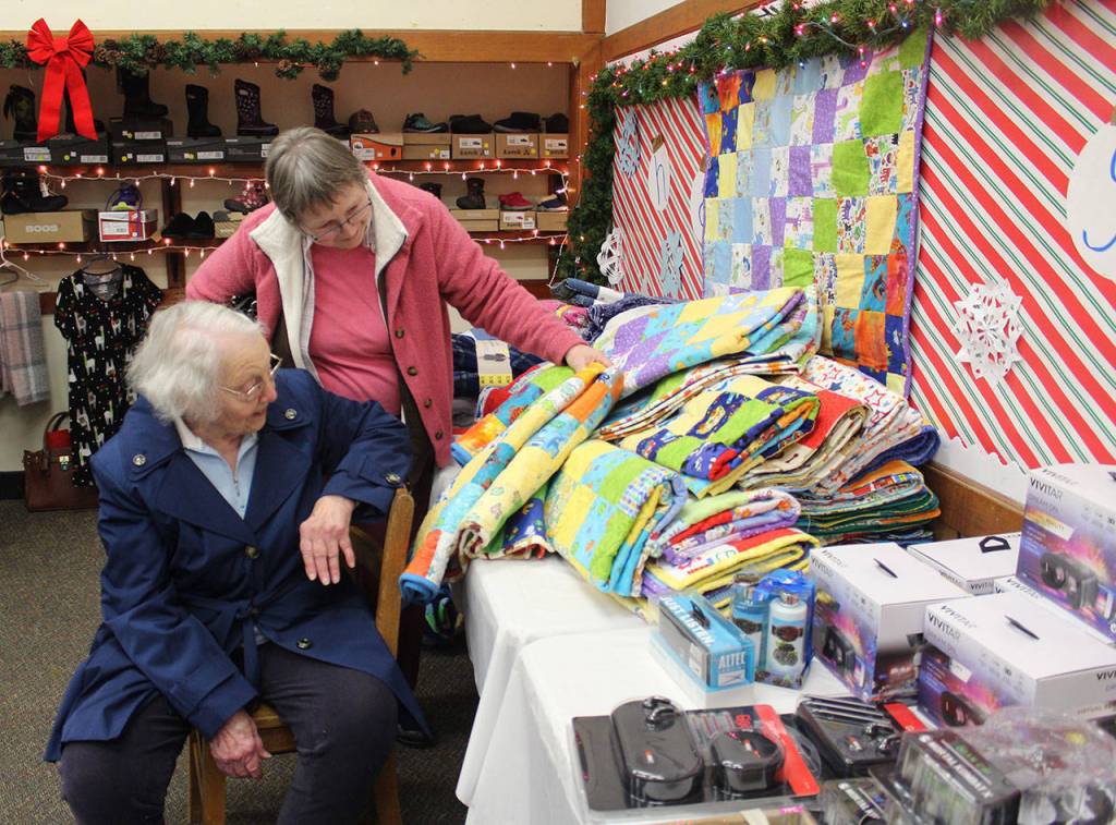 Anita Smith looks at the stacks of quilts made by Ginny Mayer. (Patricia Guthrie / Whidbey News Group)