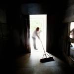 With the heavy door opened and bright morning sunlight splashing in off the granite entry, caretaker Shane Willis sweeps Rucker tomb, likely unaware of his own reflection on glass panels that protect creamation urns along the sides of the tomb. (Dan Bates / Herald Photographer)