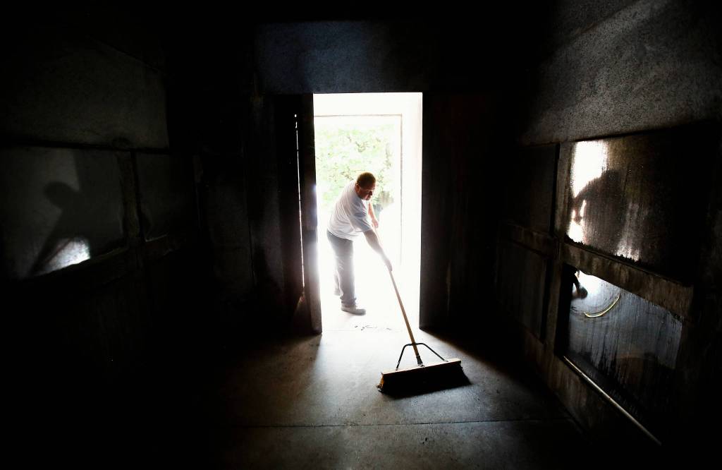 With the heavy door opened and bright morning sunlight splashing in off the granite entry, caretaker Shane Willis sweeps Rucker tomb, likely unaware of his own reflection on glass panels that protect creamation urns along the sides of the tomb. (Dan Bates / Herald Photographer)
