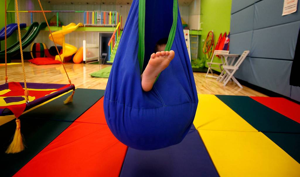Friday at Wee Fit, Hunter Standley, 6, enjoys a longer than usual moment relaxing, and that is the idea. It is called a pod swing and is soft and comfortable, as well as acting as a shield against bright light. Hunter, who has autism, is with his mom, Breanna Standley, 25, and his grandmother, Barbara Bambrick, 63. They are from Tulalip. (Dan Bates / The Herald)