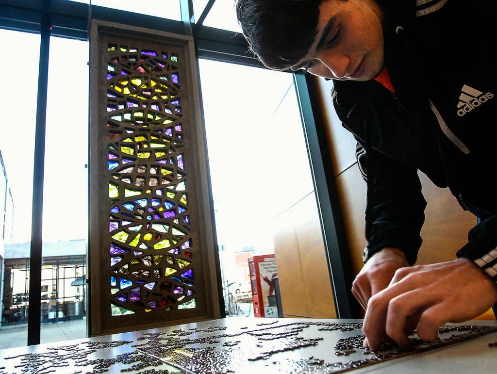 EvCC graphics design student Nathan McGinty works on a jigsaw puzzle near Russell Days untitled concrete and Blenko glass sculpture by a window in Whitehorse Hall. Day, a longtime art instructor at the college, died Monday. (Dan Bates / The Herald)