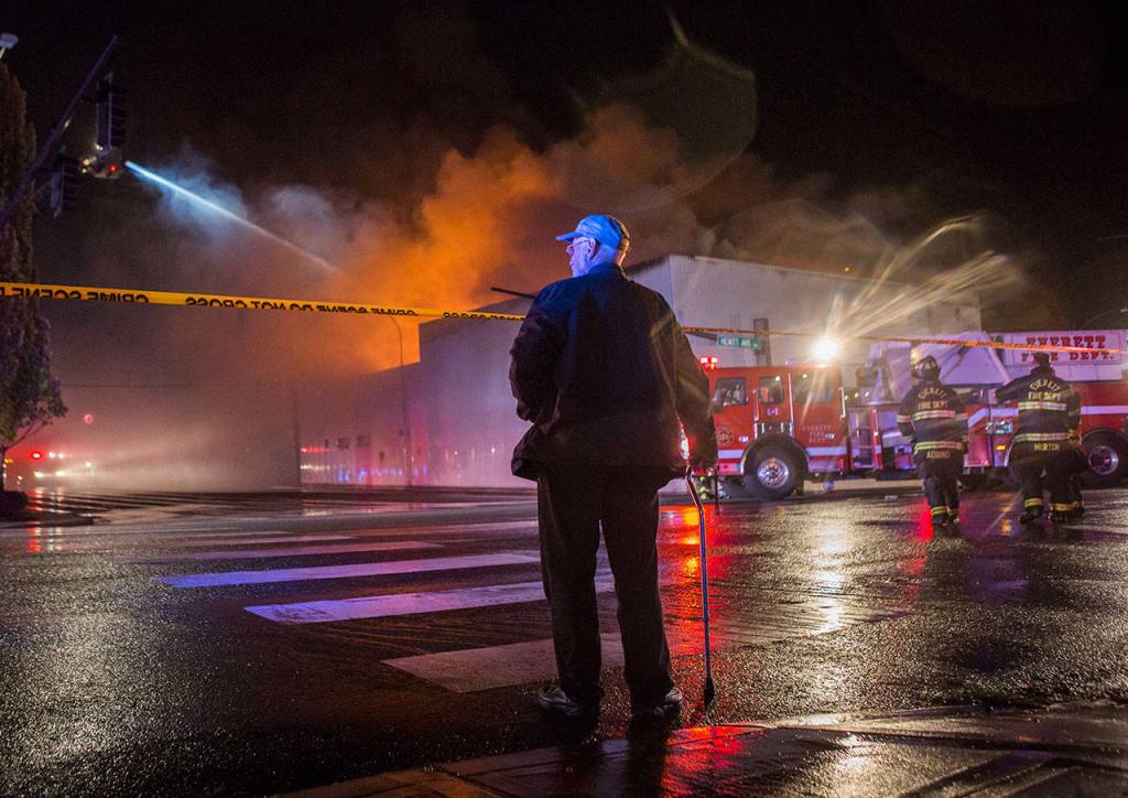 A man watches from behind police tape as the Judd & Black appliance store burns on Sept. 21, 2018, in Everett. (Olivia Vanni / Herald file)