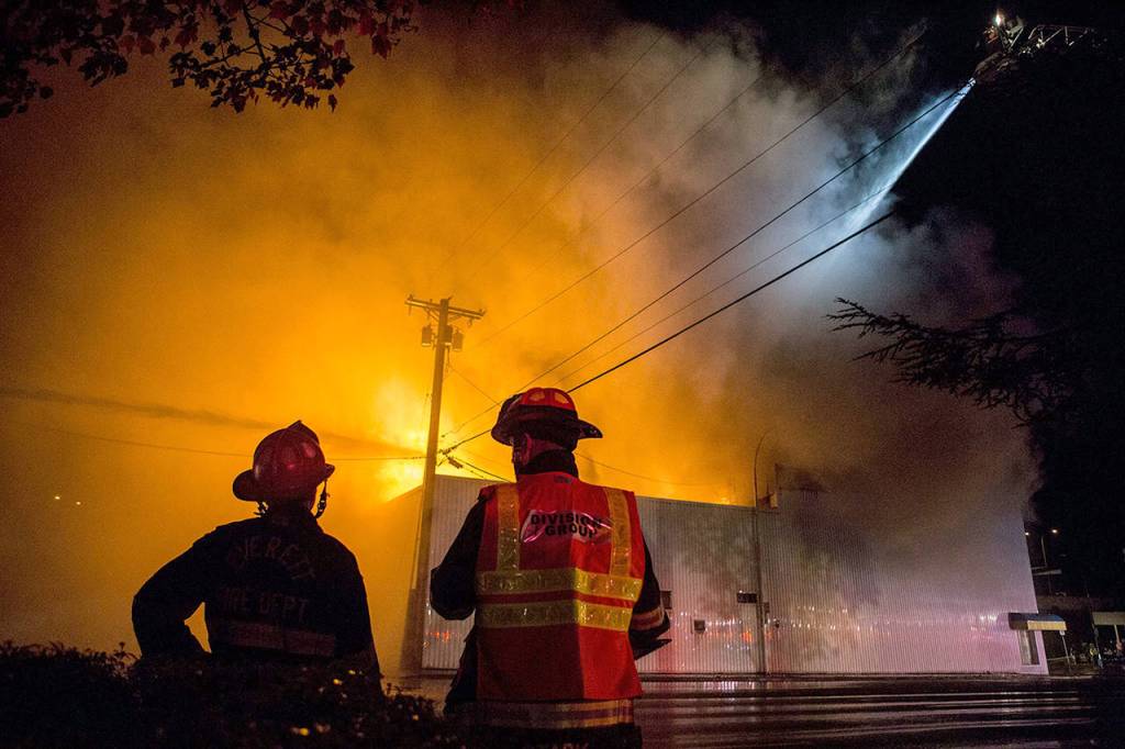 Everett Fire Department firefighters watch as water is sprayed on the Judd & Black appliance store on Sept. 21, 2018, in Everett. (Olivia Vanni / Herald file)