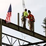 After putting the beam in place, two workers shake hands as part of the topping off ceremony for the final beam on the roof of the new YMCA building on Friday in Everett. (Andy Bronson / The Herald)