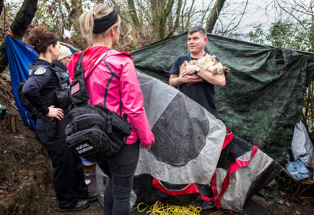 Everett Police officer Inci Yarkut (left) and COET social worker Kelli Roark (center) chat with Chris Portner (right) and his dog Gizzy at his encampment near I-5 and Marine View Drive during the annual <a href="https://www.heraldnet.com/news/annual-homeless-count-is-more-than-a-matter-of-numbers/" target="_blank">Point in Time</a> count on Jan. 23 in Everett. (Olivia Vanni / The Herald)