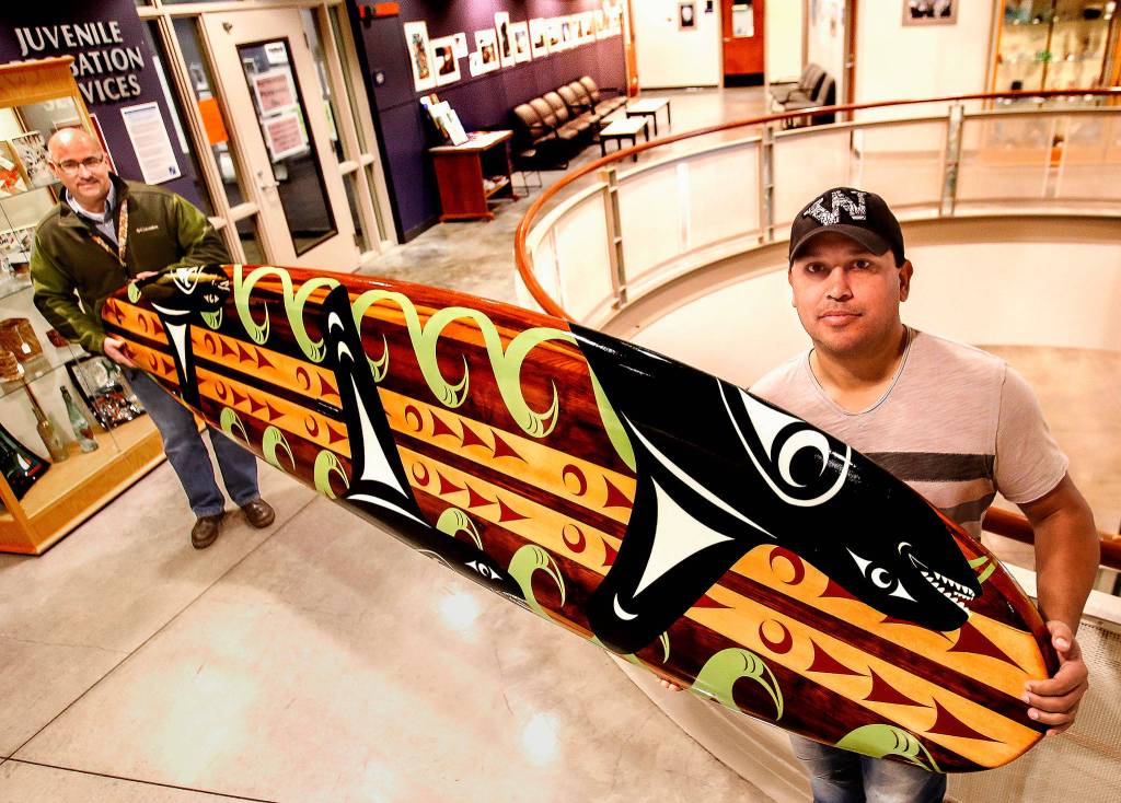At Denney Juvenile Justice Center, Snohomish County Juvenile Courts Calvin Nichols (left) and Tulalip artist James Madison bring out the paddleboard that more than 60 at-risk kids worked on for more than a year. (Dan Bates / The Herald)