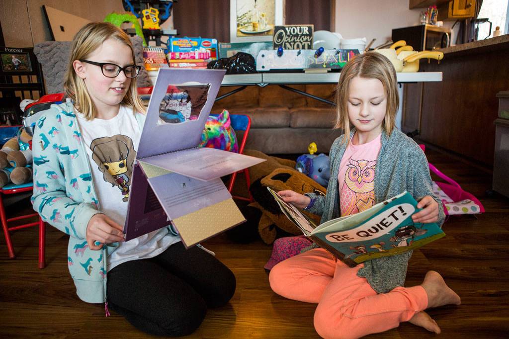 Paityn Cotterill, 10, left, and Isla Cotterill, 9, right, flip through some of their favorite books Wednesday, Feb. 6 at their home in Snohomish. (Olivia Vanni / The Herald)