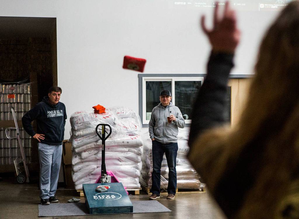 Mark Vogl (left) and Mike Diaz watch as Tera Streit throws during a cornhole game at Bosk Brew Works in Woodinville on Thursday. (Olivia Vanni / The Herald)