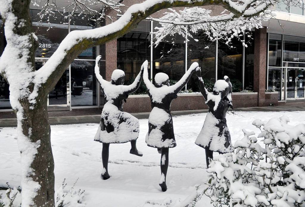 The three girls in the bronze statue Along Colby on Colby Avenue in Everett seemed to be dancing for joy in the snow Saturday morning. (Sue Misao / The Herald)