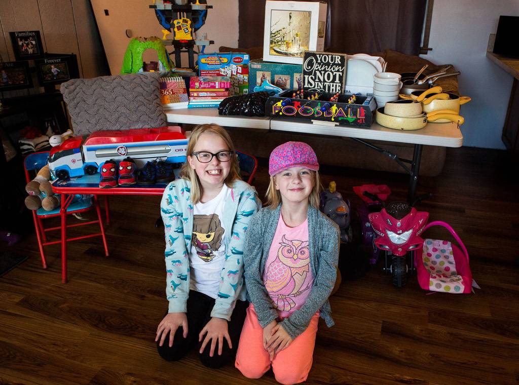 Paityn Cotterill, 10 (left), and Isla Cotterill, 9 (right), pose in front of some of their <a href="https://www.heraldnet.com/news/love-of-literature-spurs-sisters-to-stage-huge-garage-sale/" target="_blank">top-choice donations</a> at their home in Snohomish on Feb. 6. (Olivia Vanni / The Herald)