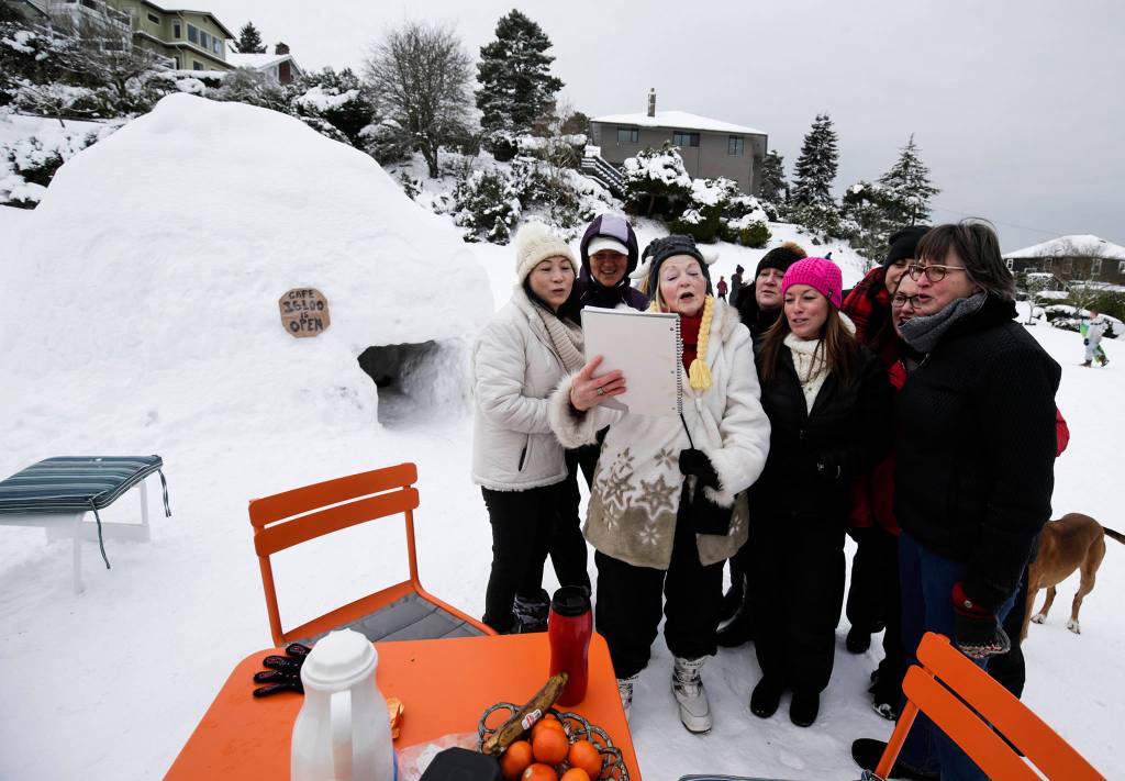 Neighbors sing the <a href="https://www.heraldnet.com/news/another-storm-brings-crashes-mounds-of-trash-and-an-igloo/" target="_blank">Igloo Hut Song</a> at Rucker Park on Feb. 11 in Everett. The song was written by Cherie Hansen (center) and sung to the tune of O Christmas Tree. (Andy Bronson / The Herald)