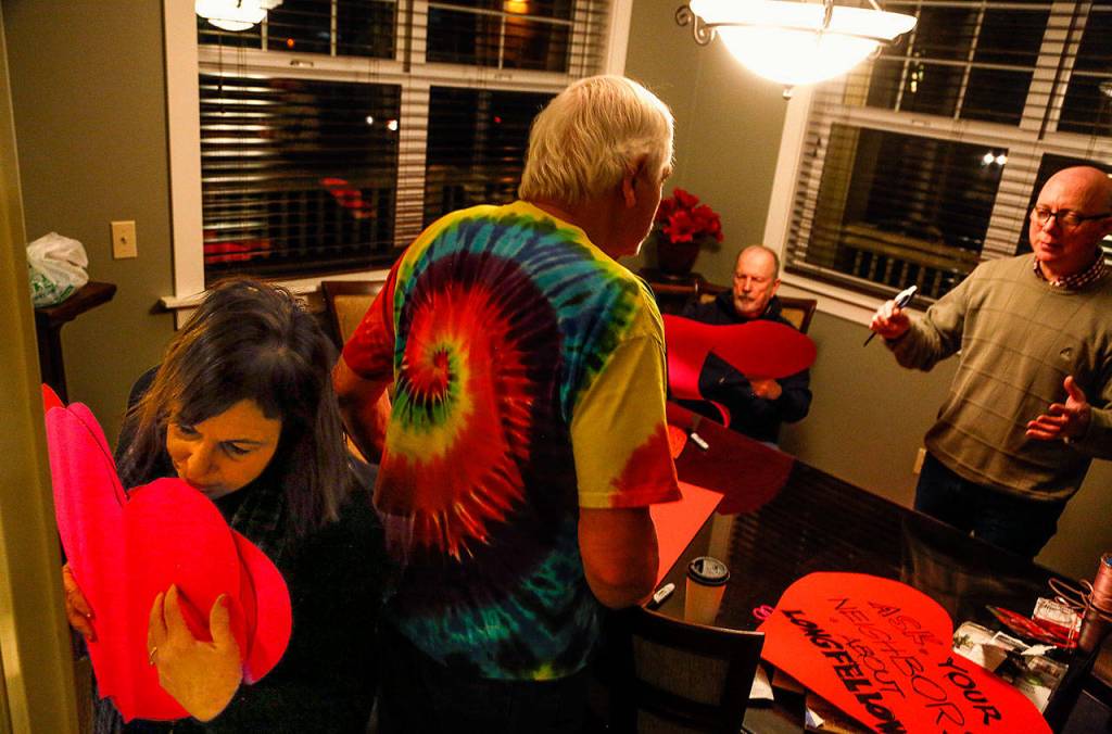 Carrying a stack of hearts, Andrea Tucker squeezes past Paul Popelka, who is talking with Patrick Hall. Jack ODonnell (sitting) is cutting out more hearts for Fridays heart-bombing to raise awareness of plans to demolish Everetts old Longfellow School. (Dan Bates / The Herald)