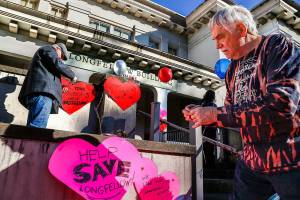 Local preservationists Paul Popelka (right) and Patrick Hall attach paper hearts with messages about the Longfellow Building in Everett Friday. They are heart-bombing the 108-year-old former school to raise awareness of plans to demolish it for parking. (Dan Bates / The Herald)