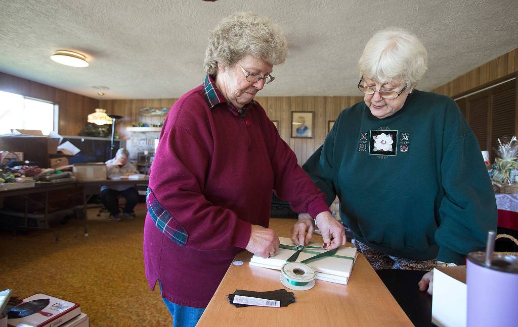 Darlene Strotz wraps a three-book set about the history of Stanwood, as Korene Thomas lends a finger. Theyve used this week to organize, label and catalog items for the Silvana Fair Board Auction on Saturday. (Andy Bronson / The Herald)