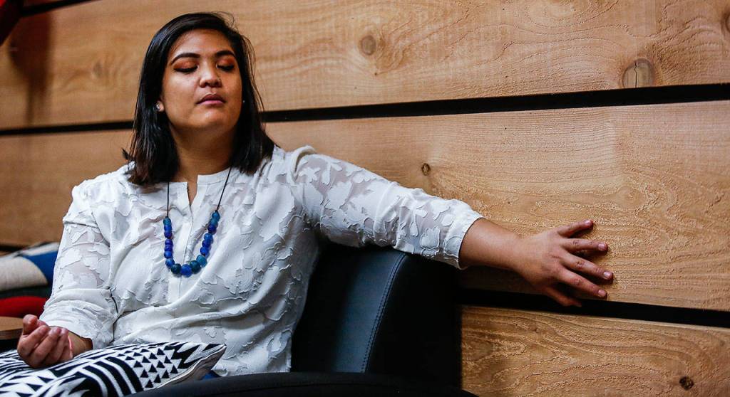 Emma Kaahaaina, program manager of EvCCs Diversity & Equity Center, feels the texture of a heavy cedar plank lining a wall in a new space for Native American, Indigenous and Pacific Islander students on campus. The cedar, milled in Oso, gives the space a feeling of being in a longhouse. (Dan Bates / The Herald)