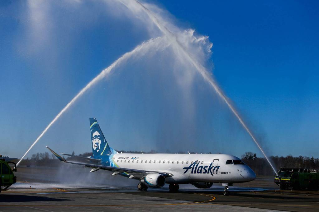 The first flight makes its way under a celebratory water arch send-off during the grand opening of Paine Field Airport on March 4 in Everett. (Olivia Vanni / The Herald)
