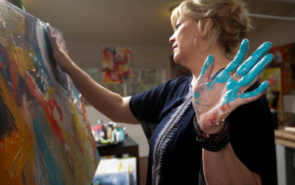 Blue paint coats one of Corts hands as she paints in her Snohomish studio. (Andy Bronson / The Herald)