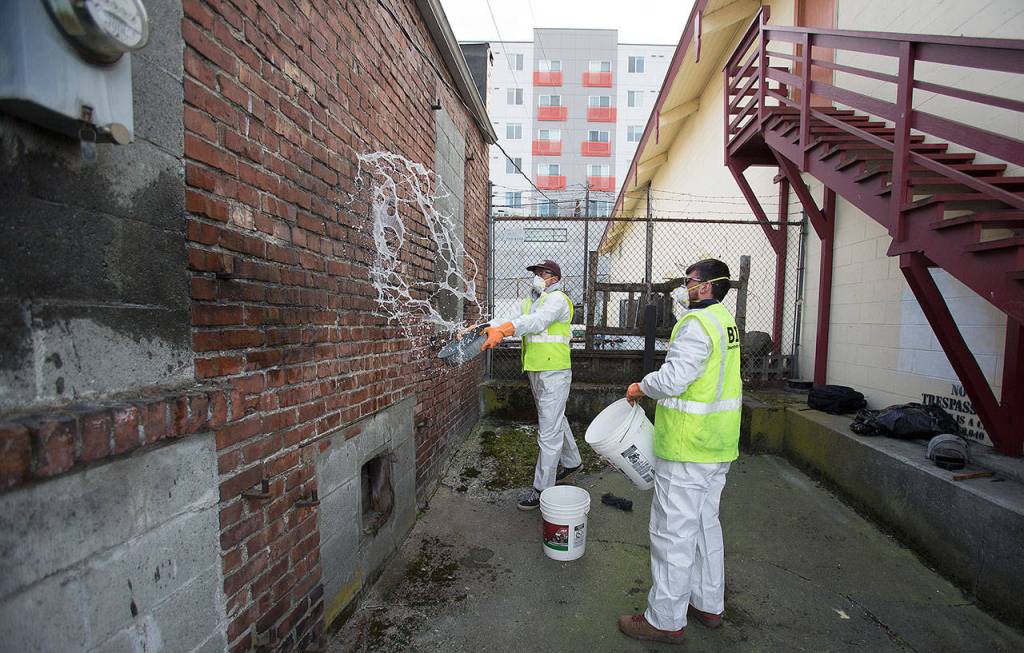 Business Improvement Associations Trevor Dodge splashes water on a wall just cleaned of graffiti at Charlies Combat Club in downtown on Thursday, March 21, 2019 in Everett, Wash. Cody MacDouglal waits to use a second bucket of water to finish the cleaning. (Andy Bronson / The Herald)