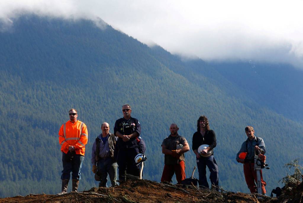 Workers listen as a bagpiper plays during a moment of silence at 10:37 a.m. on April 12, 2014, three weeks after the fatal mudslide in Oso. (Annie Mulligan / For The Herald)