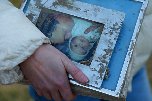 A woman holds family photos pulled from the rubble the day after the fatal mudslide near Oso. (Genna Martin / The Herald)