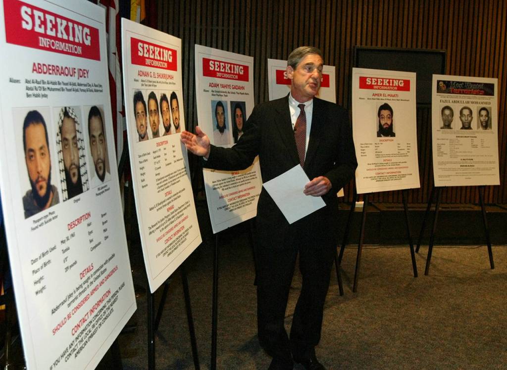 FBI Director Robert Mueller talks to reporters in front of posters of individuals sought in connection with possible terrorist threats against the United States during a news conference with Attorney General John Ashcroft at FBI Headquarters on May 26, 2004. (AP Photo/Charles Dharapak, file)
