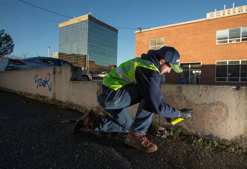 As a member of the Business Improvement Association crew, Cody McDougall cleans up multiple graffiti marks along a wall in downtown on March 18, 2019 in Everett. (Andy Bronson / The Herald)