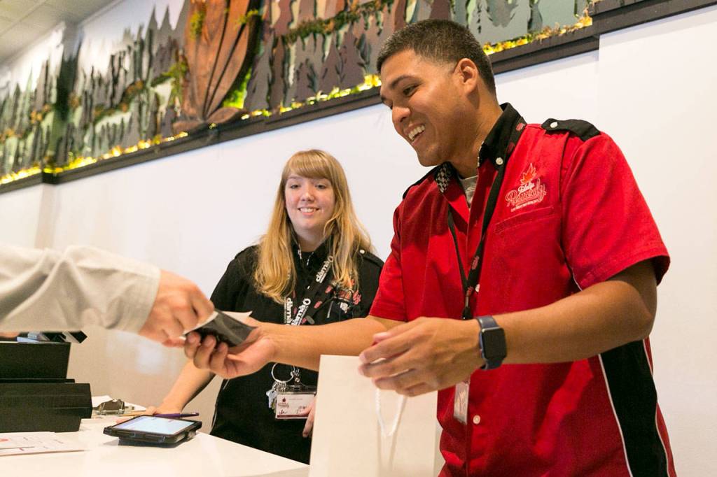 Tyana Green (left) watches as Juan Martinez hands over a purchase to a customer of Remedy Tulalip on Aug. 22, 2018. (Kevin Clark / Herald file)