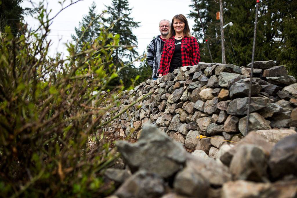 Tim Robinson and his wife Julie Ross-Robinson next to the rock wall at their home in Bothell. (Olivia Vanni / The Herald)