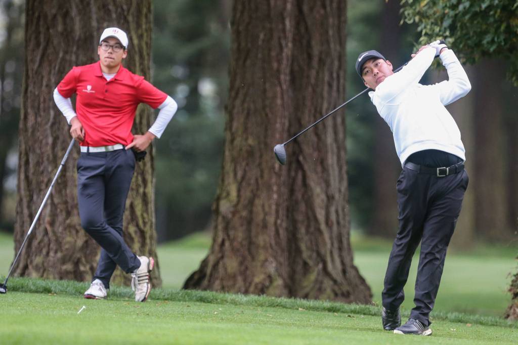 St. Georges Riley Lai (left) watches as Kamiaks Alvin Kwak tees off during the Tom Dolan Memorial Invitational golf tournament Monday afternoon at Everett Golf & County Club in Everett on April 8, 2019. (Kevin Clark / The Herald)