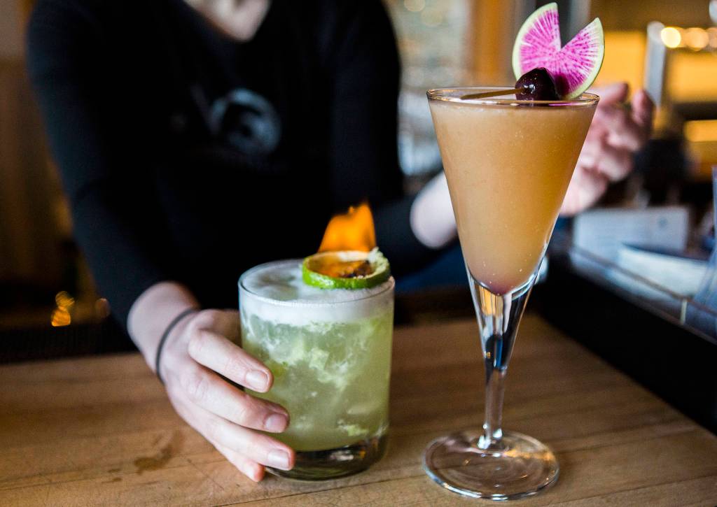 Two of Bluewater Distillings current cocktails, Burning Love (left), made with house gin, mezcal, grapefruit juice, lime juice, raw simple syrup, house amaretto and house-made tiki bitters and The New Sling (right), made with organic Winter Sun Aquavit, rum, passionfruit nectar, lime juice, muddled cucumber and peach bitters are displayed at the Bluewater Distilling bar on April 4 in Everett. (Olivia Vanni / The Herald)
