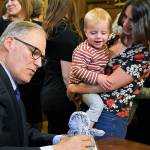 Nikki Dziedzic and her two-year-old son Jude look on as Gov. Jay Inslee props up Judes stuffed penguin while signing HB 1870 on April 17. (Office of the Governor photo)