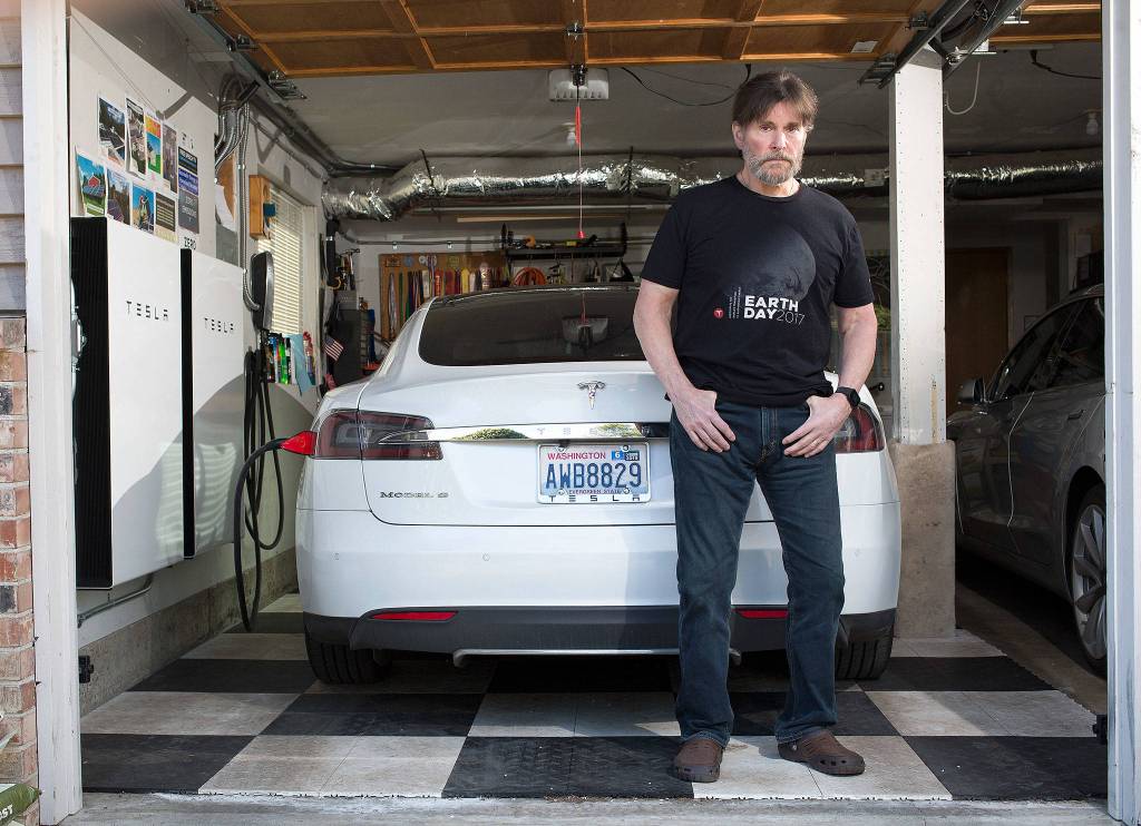 David Kendall stands in front of one of two Tesla cars and two Tesla Powerwall 2 batteries hanging in his garage. (Andy Bronson / The Herald)