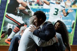 Seattle Seahawks quarterback Russell Wilson, center, hugs head coach Pete Carroll, left, in front of a photograph of Wilson in action, as Wilsons wife Ciara looks on at right, Wednesday, April 17, 2019, prior to a NFL football press conference in Renton, Wash. Earlier in the week, Wilson signed a $140 million, four-year extension with the team. (AP Photo/Ted S. Warren)