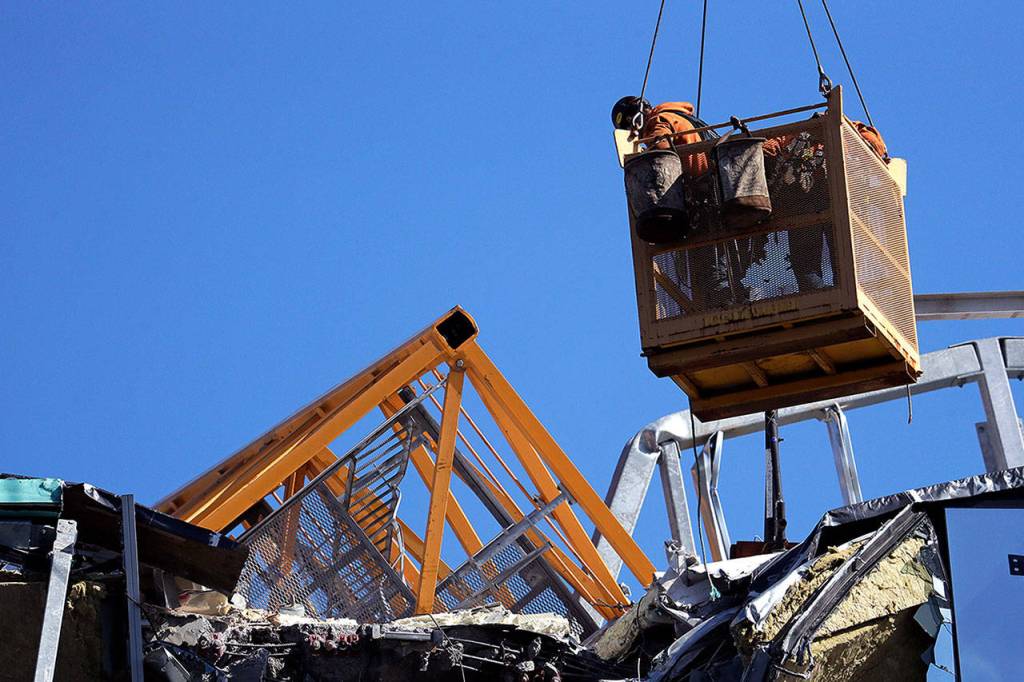 With a portion of the broken crane on the roof behind, workers suspended in a basket on Sunday look at debris from a building damaged when the crane atop it collapsed a day earlier in Seattle. (AP Photo/Elaine Thompson)