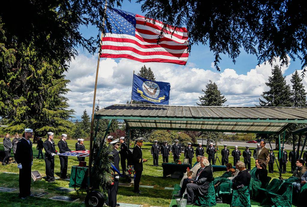 A chaplain from Naval Station Everett, Lt. Jisup Choi, leads the memorial service for Seaman 1st. Class Daniel Guisinger Jr. beneath a covered seating area at Cypress Lawn Memorial Park in Everett on April 27. (Dan Bates / The Herald)