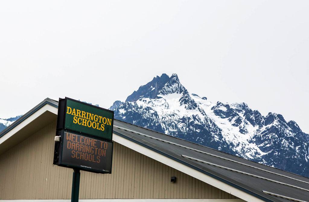 Mountains can be seen behind a <a href="https://www.heraldnet.com/news/darrington-takes-care-of-its-own-school-superintendent-says/" target="_blank">Darrington Schools</a> sign marking the campus area for Darrington High School and Darrington Elementary on April 25. (Olivia Vanni / The Herald)