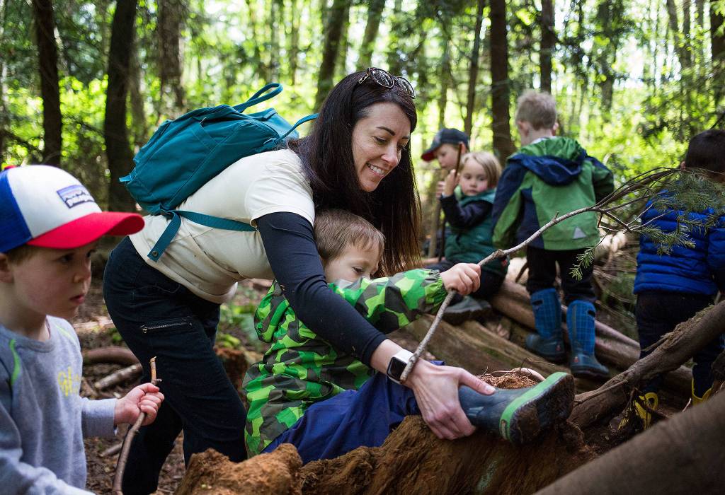 Kristin Hammer, owner of Nature Together, helps a stuck Lincoln Mays, 3, climb out of a tree stump in an area called the kids call the pirate ship in Japanese Gulch Park on May 1 in Mukilteo. The preschool specializes in day classes with an environment theme. (Andy Bronson / The Herald)