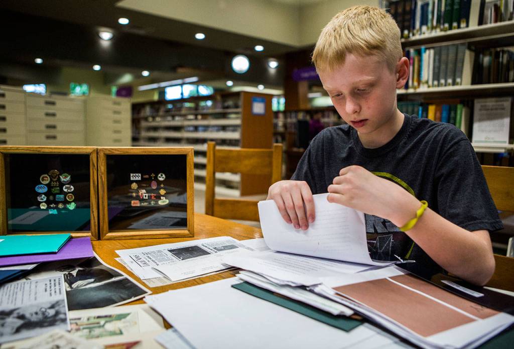 Spencer Armstrong searches through the piles of information he has gathered on Willis D. Tucker at the Snohomish Library. (Olivia Vanni / The Herald)